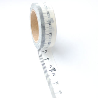 A washi measuring tape with some of the tape rolled out and stuck on a plain background